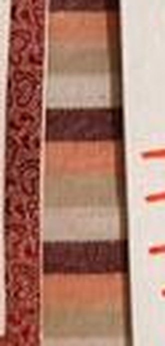 Close view of a vision board edge: red glitter border on white card, resting on a striped bedsheet.