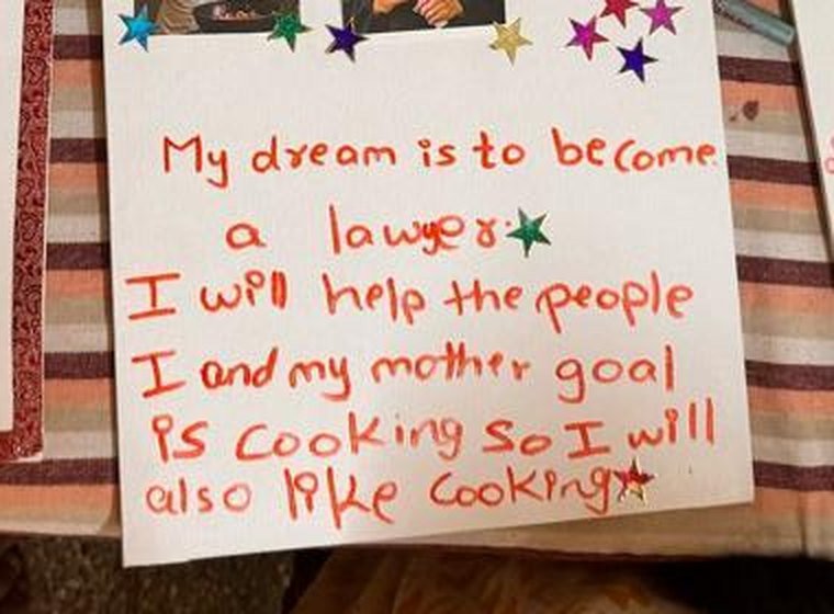 A child's vision board on a striped bedsheet, reading: My dream is to become a lawyer. I will help the people. And my mother goal is cooking so I will also like cooking.